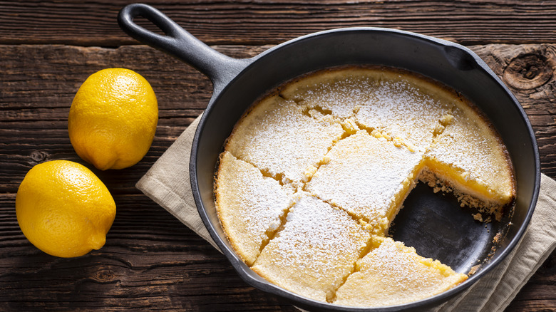 Lemon bars in a cast iron skillet next to whole lemons