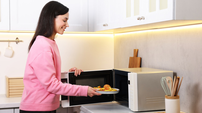 Woman placing plate of food in microwave