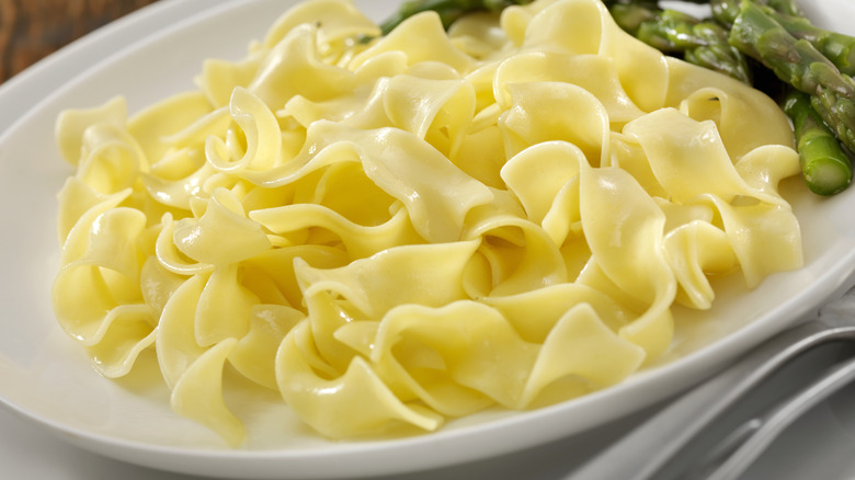 a plate of egg noodles with butter and steamed asparagus.