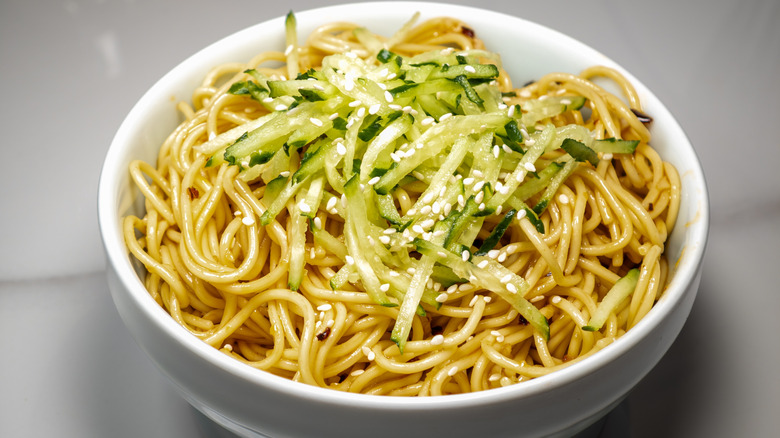 cold sesame noodle salad with shredded cucumber in a white bowl.