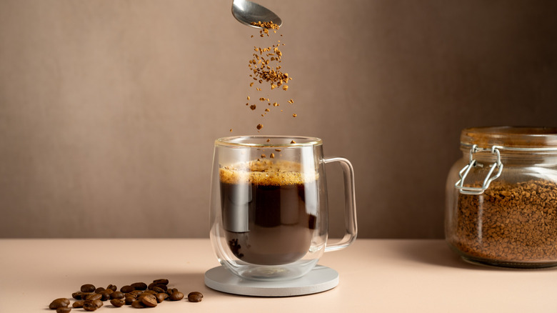 small cup of coffee in glass mug with sprinkle of coffee beans