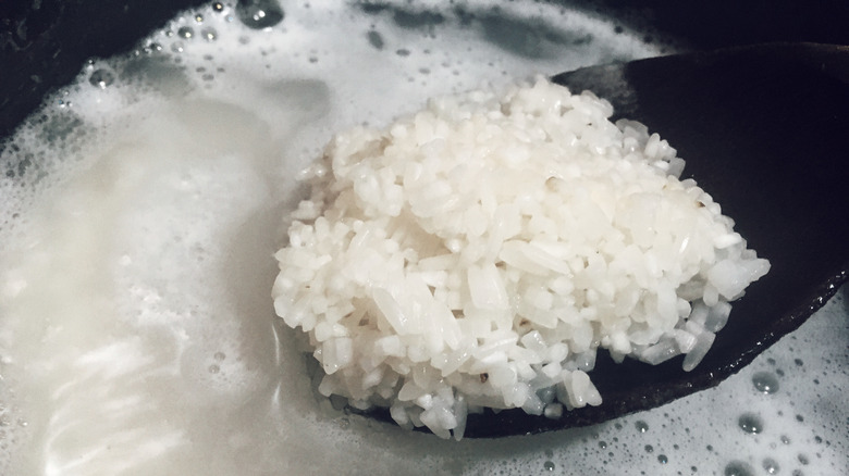 Close up of spoonful of rice in a pot of water