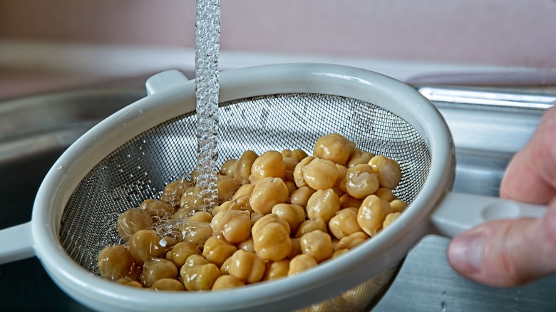 Hand holding colander with chickpeas under stream of water