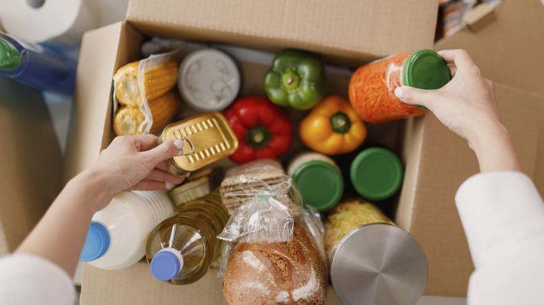 Hands pulling items out of a box filled with fresh produce and other food