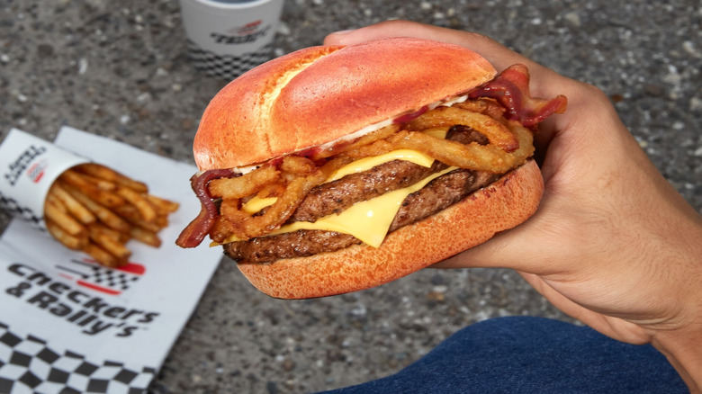 Checkers and Rally's Barbecue Pretzel Buford being held by someone with fries and a drink on the ground.