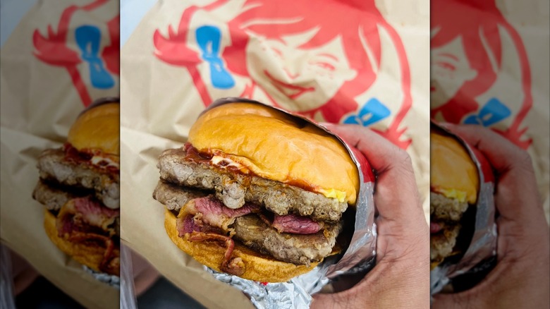 A hand holds a Wendy's burger.