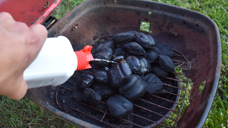 Hand squirting lighter fluid on coals