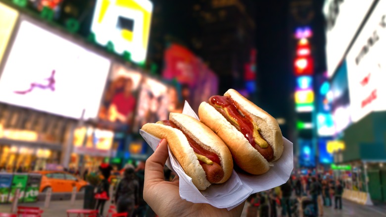 two hot dogs in one hand on a busy NYC street
