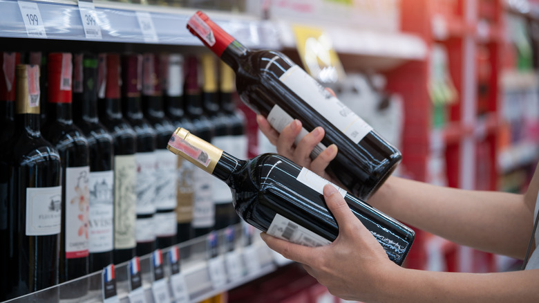 A person choosing between two bottles of red wine