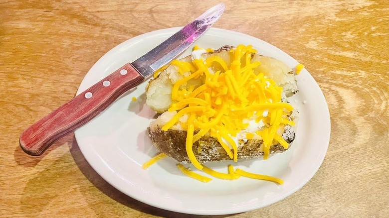 Texas Roadhouse's Baked Potato with a steak knife and shredded cheese on top