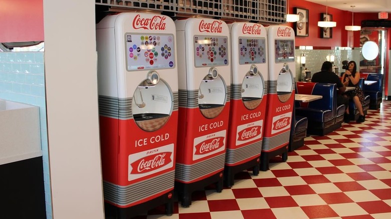 Four Coca-Cola Freestyle machines stand in a row in a diner.
