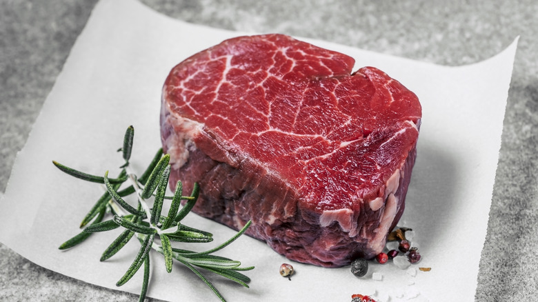A filet mignon on a table with a sprig of rosemary