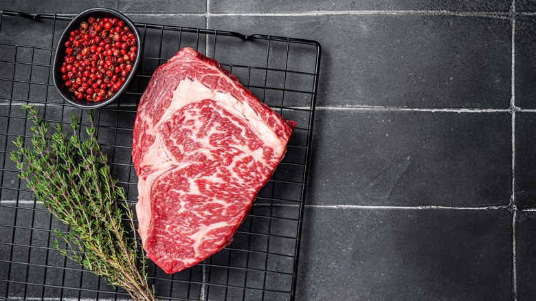 A ribeye steak on a wire rack alongside thyme