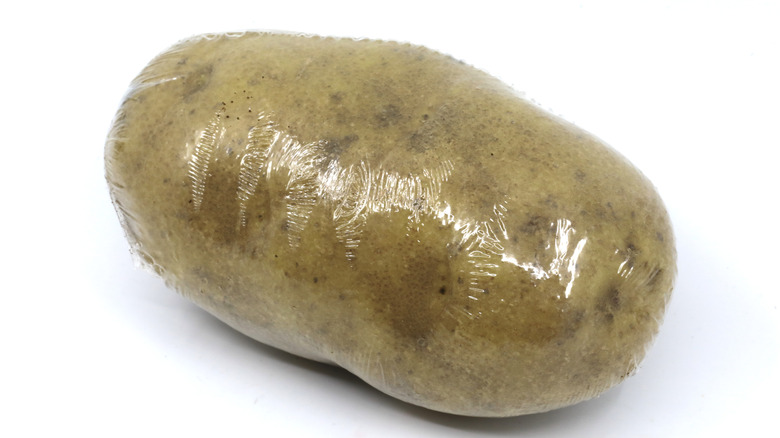 A lone individually plastic-wrapped potato sits on a white background