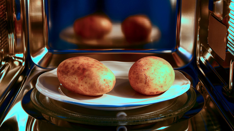 Two whole potatoes sit in a microwave on a plate