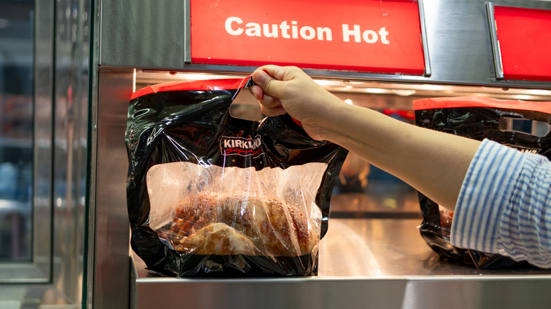 A shopper picks up a rotisserie chicken from Costco.