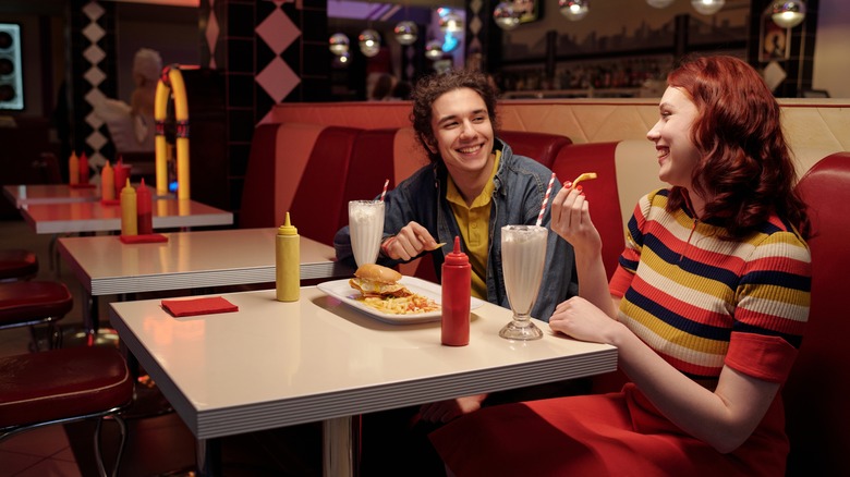 Two young people share fries and milkshakes in a diner