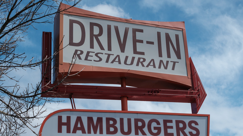 Vintage sign for a drive-in restaurant against a blue sky with clouds
