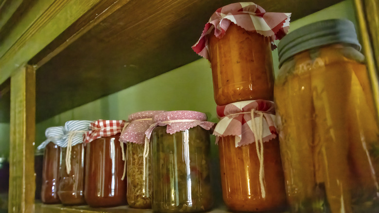 Jars of preserved food line a wooden shelf