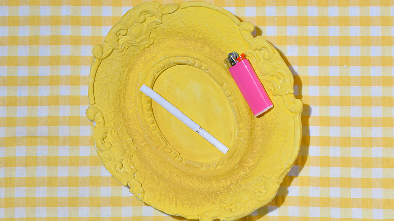 A cigarette and lighter lie on a bright yellow plate on a yellow gingham tablecloth