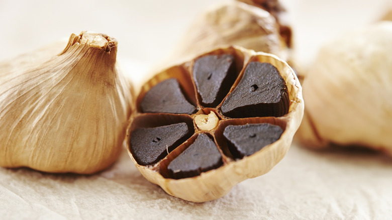 Head of black garlic cut in half showing black cloves inside, with several whole garlic heads next to it