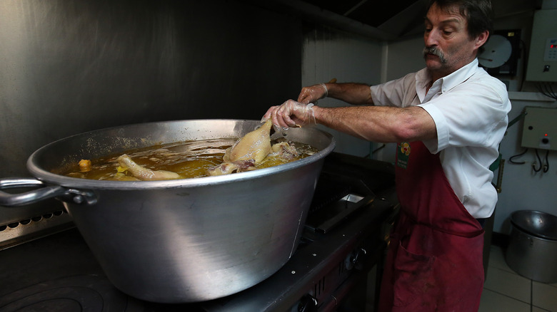 Cook putting bird legs into pot of fat