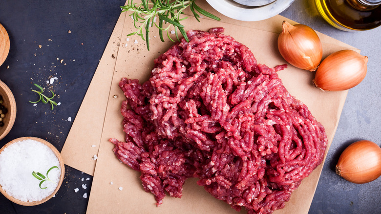 Ground beef on brown butcher paper next to onions and salt
