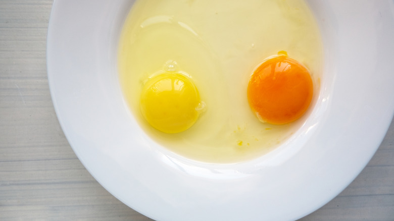 Two different colored egg yolks sit with combined whites on a white plate