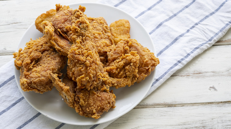 a plate of fried chicken on a white and blue-striped hand towel and white wood table