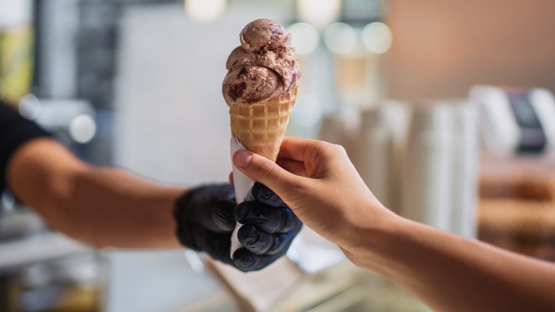 Vendor passing chocolate ice cream cone to customer