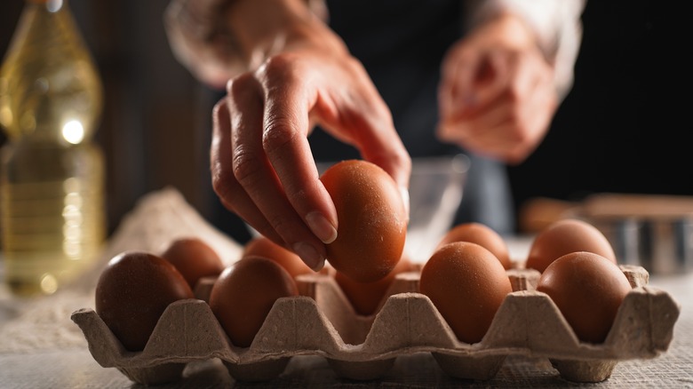 A baker reaches for an egg out of a carton