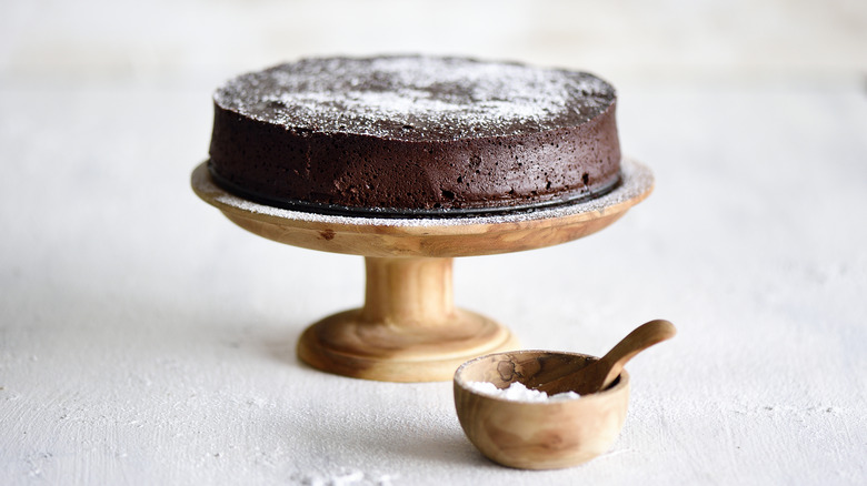 A flourless chocolate cake sits on a wooden cake stand