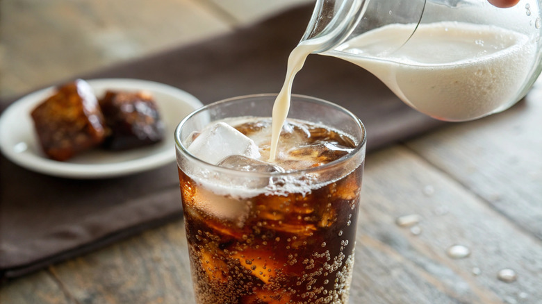 Someone pours milk into a glass of cola.