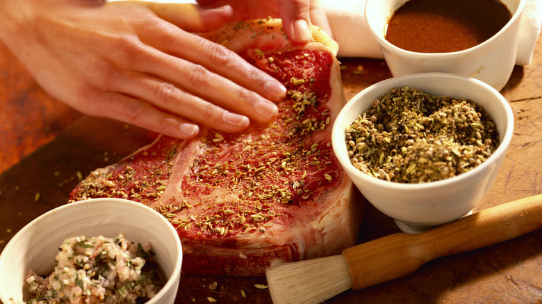 Hands rubbing seasoning on a raw steak in the kitchen