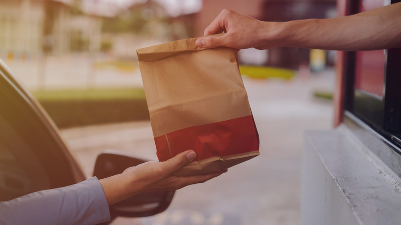 A drive-thru worker passes a bag of food to a person in a car