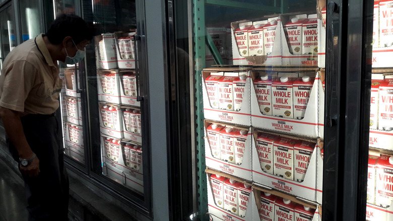 A man in a darkened Costco examines the refrigerator with milk