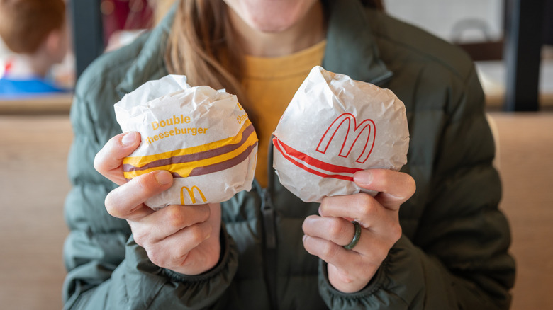 Someone holds up two McDonald's burgers packaged in paper wrappers.