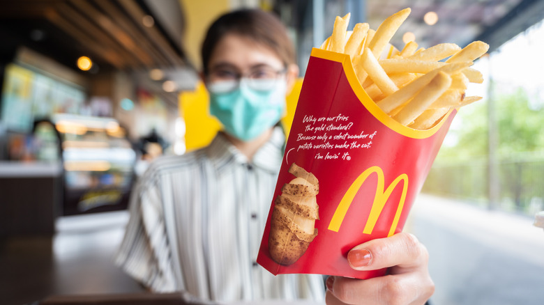 A masked McDonald's worker holds out a box of french fries.