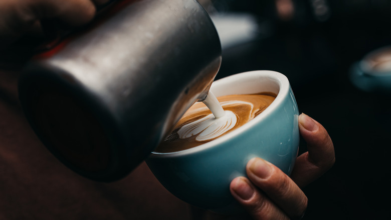 Pouring steamed dairy into coffee in blue cup