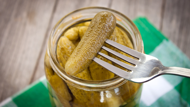 Fork picking out cornichon from jar