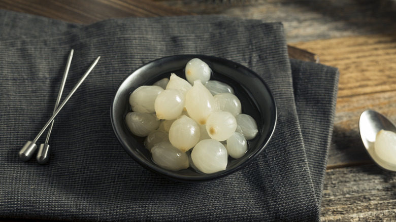 Black bowl of cocktail onions next to cocktail picks
