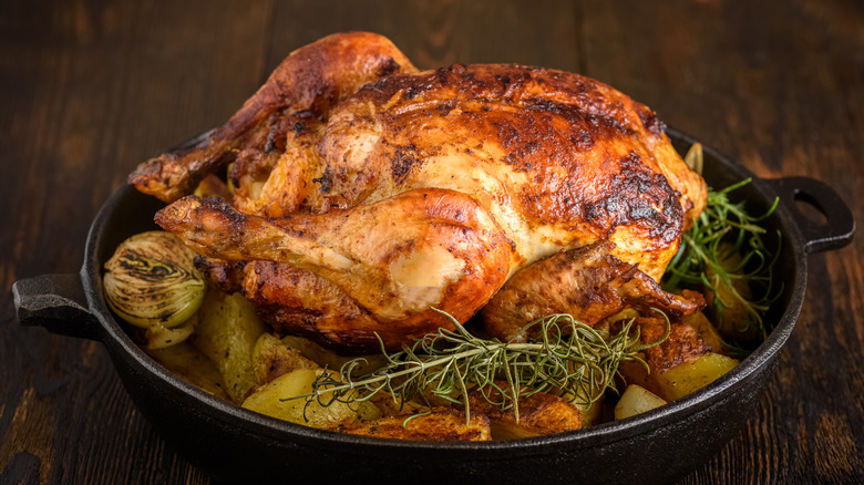 A beautifully roasted chicken sits on a bed of potatoes in a cast iron skillet