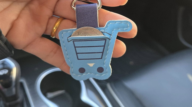 A hand holding an Aldi quarter-keeper shaped like a shopping cart