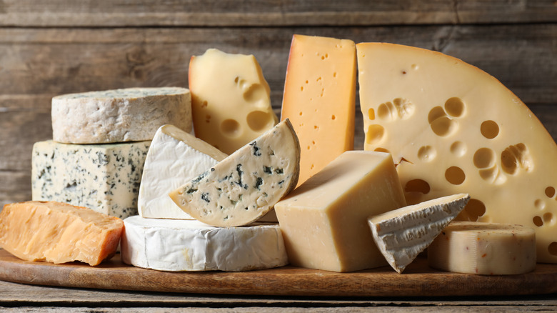 Different types of cheese sit on a wooden cutting board.