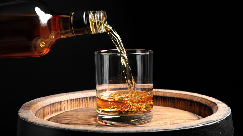 Glass of whiskey on a barrel being poured from a bottle