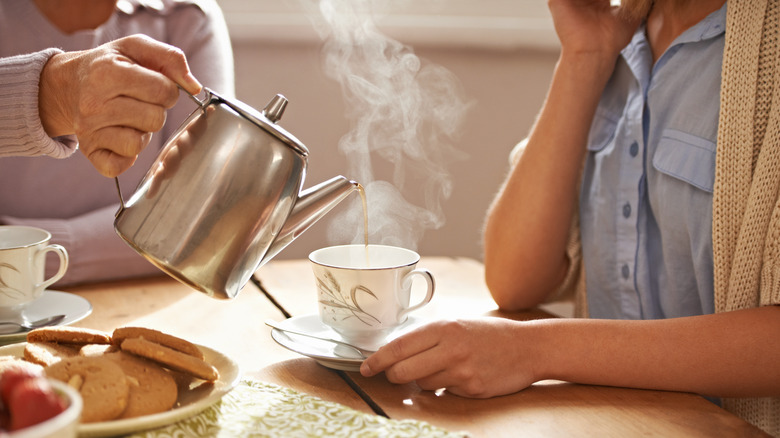 person serving steaming tea into cup