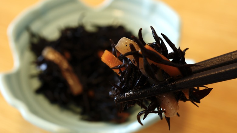 Chopsticks holding a biteful of seaweed and shaved carrots