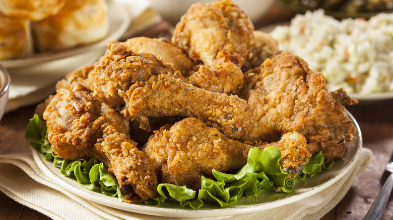 A plate of American-style fried chicken served on a bed of lettuce next to various side dishes