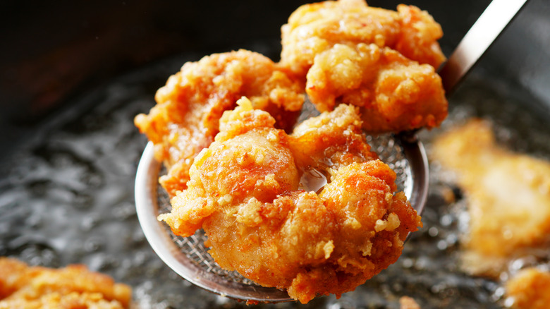 A piece of Japanese fried chicken, known as karaage, held above hot oil in a draining spoon