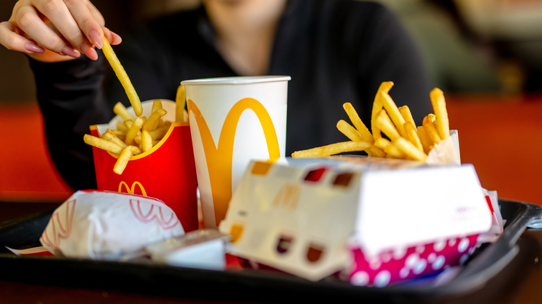Woman eating McDonald's fries and a tray with burgers and a soda